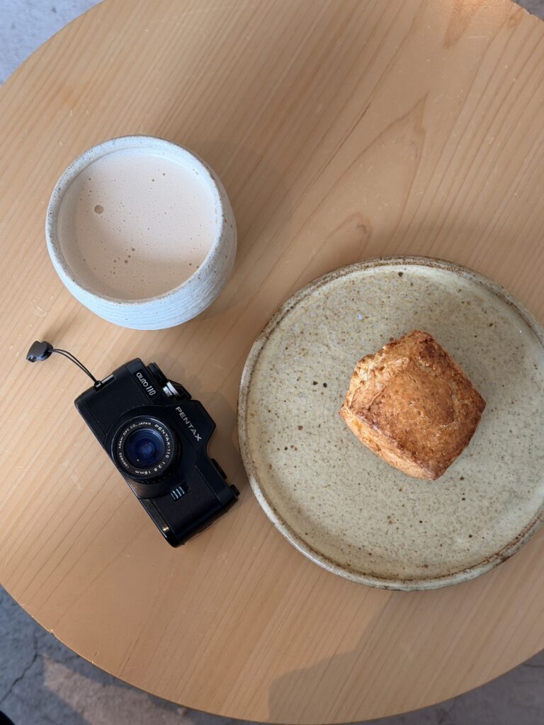 Camera put on a table along with a cup of coffee and bread.