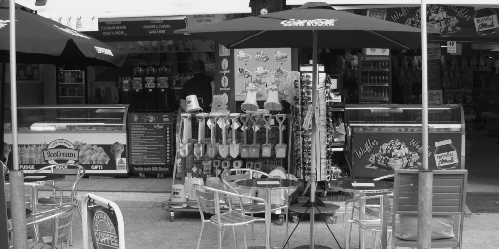 Monochrome image showing exterior of shop with tables and chairs, merchandise